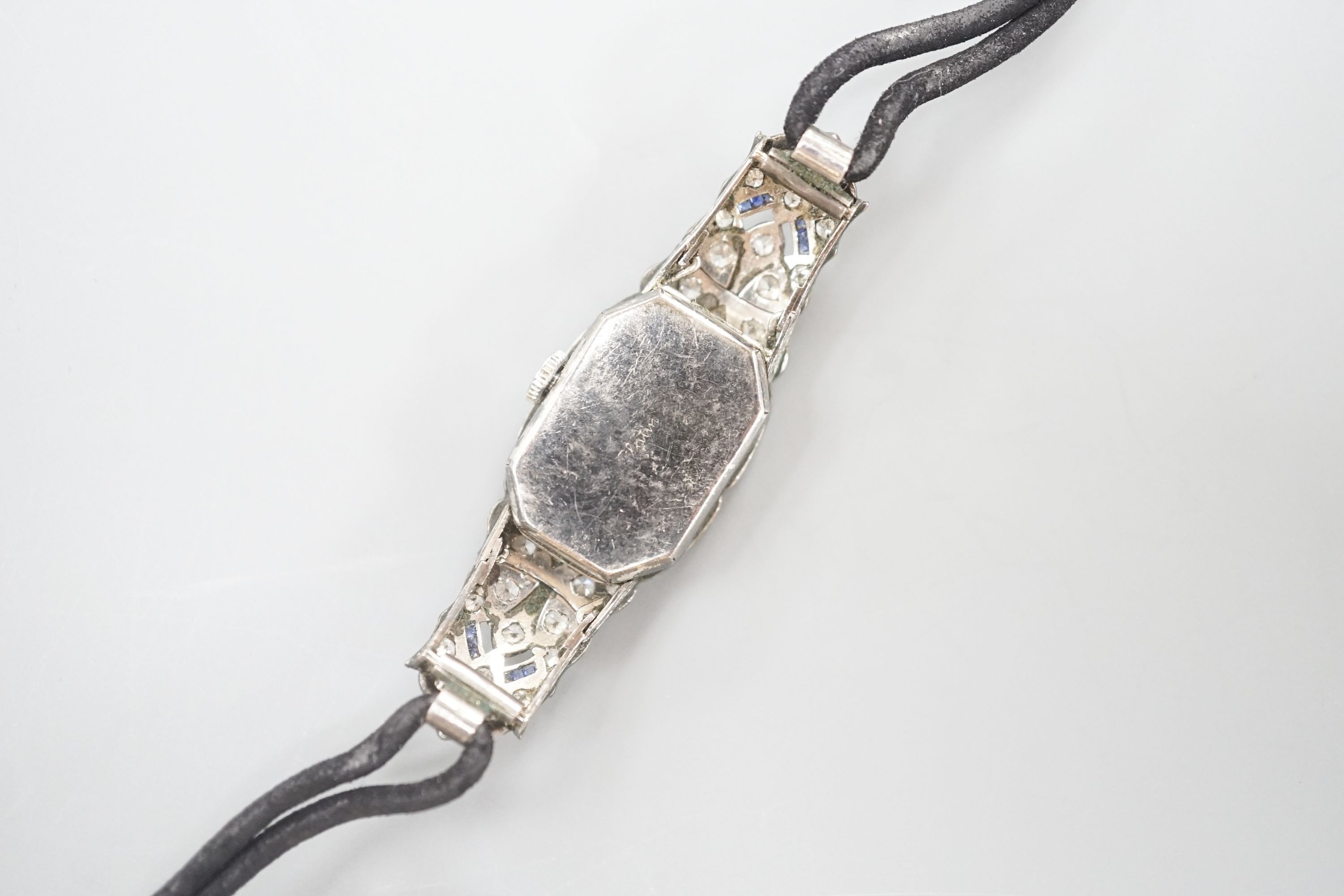 A lady's mid 20th century engraved white metal, diamond and sapphire set cocktail watch, case diameter 17mm, gross weight 18.3 grams, on a later? twin strand fabric strap.